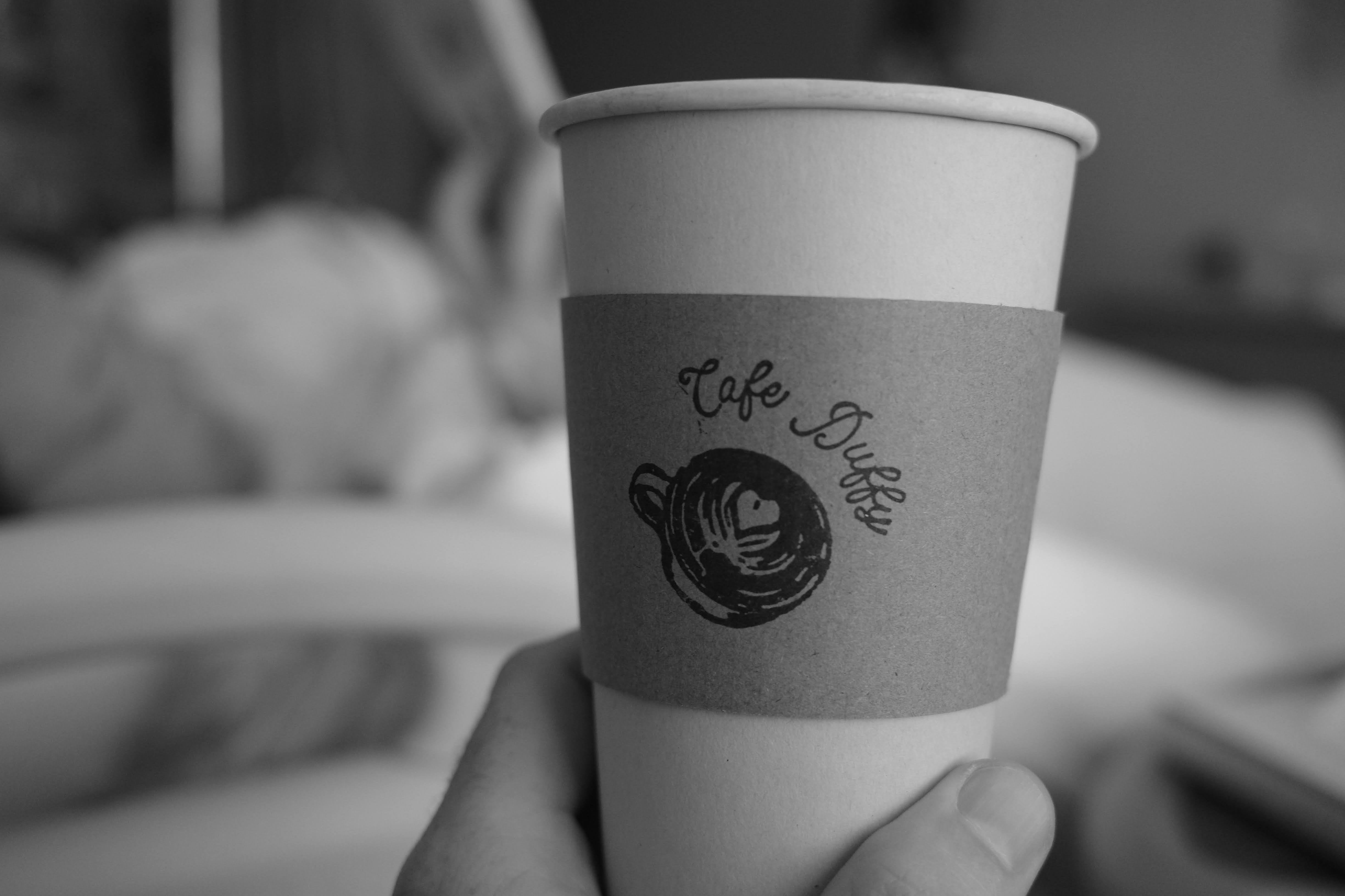 Paper coffee cup that says “Cafe Duffy” with a black coffee cup logo under it